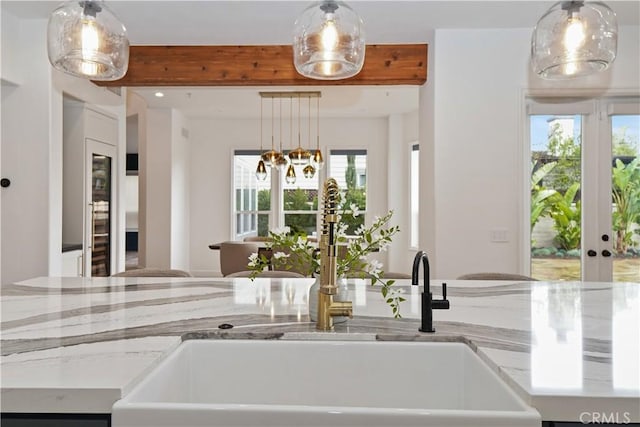 kitchen with sink, decorative light fixtures, light stone countertops, and beamed ceiling