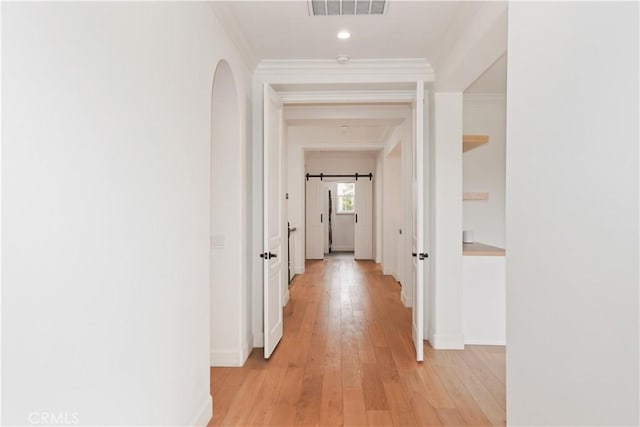 hall with light hardwood / wood-style flooring, ornamental molding, and a barn door