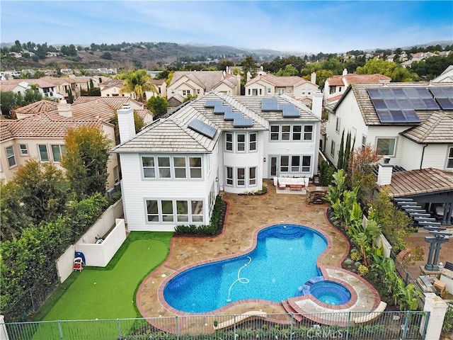 rear view of property with a pool with hot tub, a patio, and solar panels