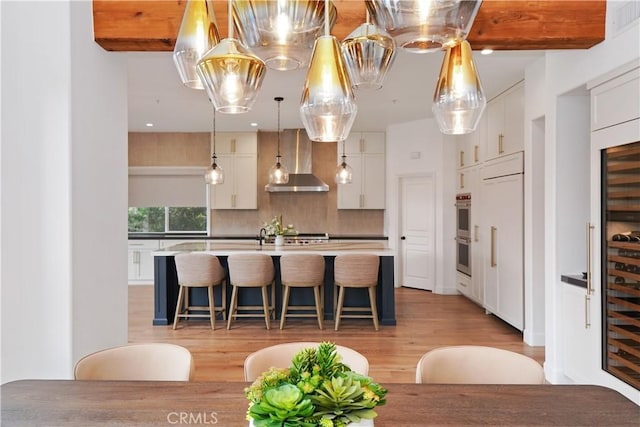 kitchen featuring hanging light fixtures, white cabinets, decorative backsplash, wall chimney exhaust hood, and light wood-type flooring