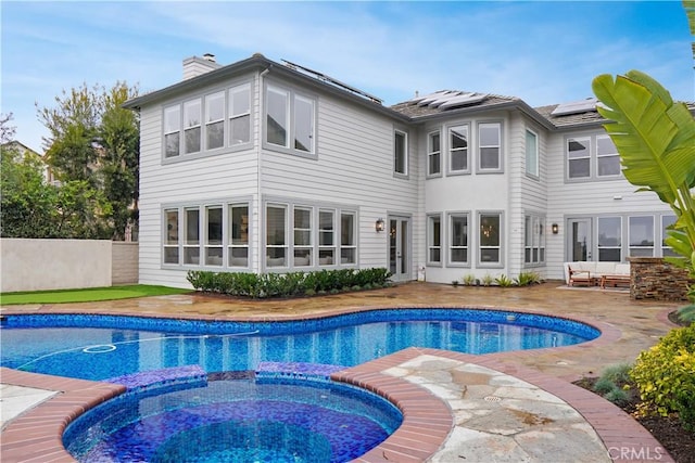 back of house featuring a swimming pool with hot tub, an outdoor living space, a patio, and solar panels