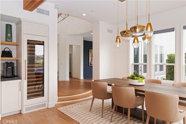 dining space featuring wine cooler, a chandelier, light hardwood / wood-style flooring, and beamed ceiling