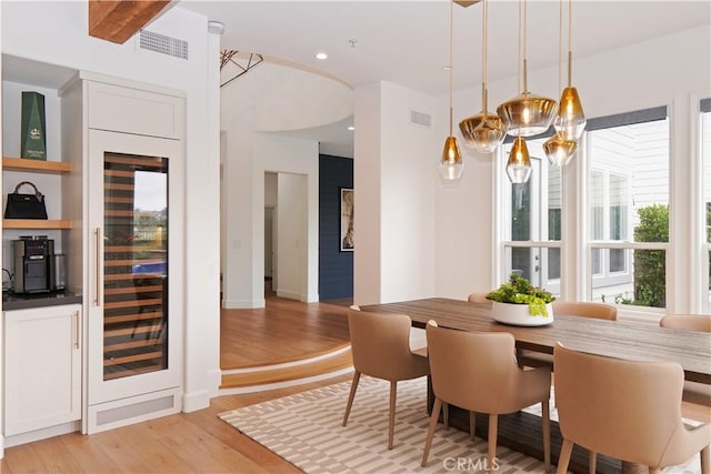 dining area with a chandelier, visible vents, beverage cooler, and light wood-style floors