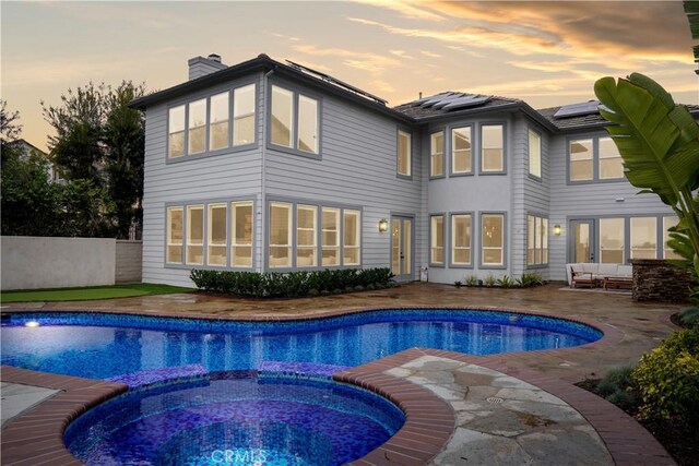 back house at dusk featuring a swimming pool with hot tub, a patio area, outdoor lounge area, and solar panels