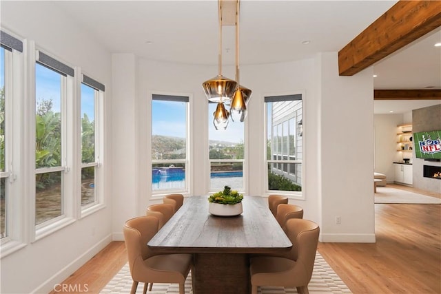 dining area featuring beamed ceiling, a fireplace, and light hardwood / wood-style floors