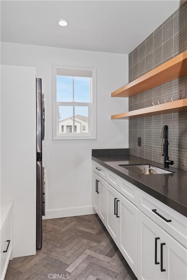 kitchen with a sink, backsplash, dark countertops, and white cabinetry