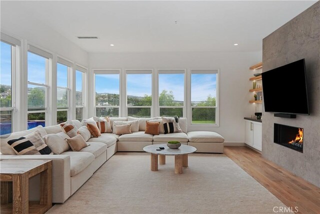 living area featuring recessed lighting, visible vents, a large fireplace, and light wood finished floors