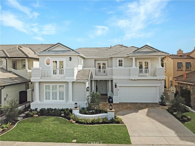 view of front of home with french doors, concrete driveway, an attached garage, a balcony, and a front lawn