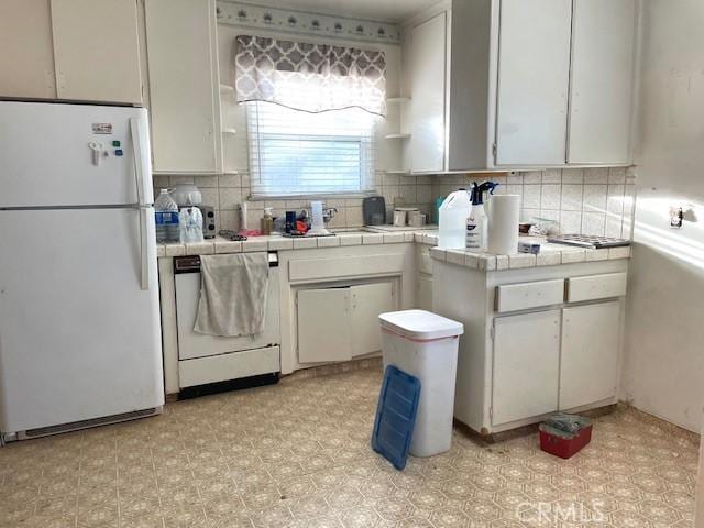 kitchen with white refrigerator, white cabinetry, and tile counters