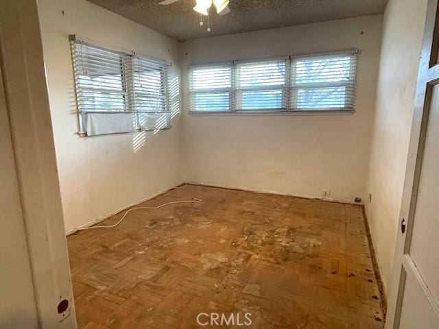 empty room with parquet floors, ceiling fan, and a textured ceiling