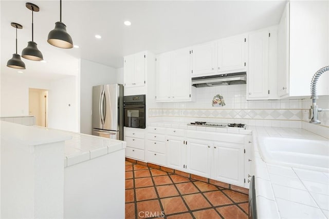 kitchen featuring gas cooktop, tile counters, stainless steel fridge, oven, and white cabinets