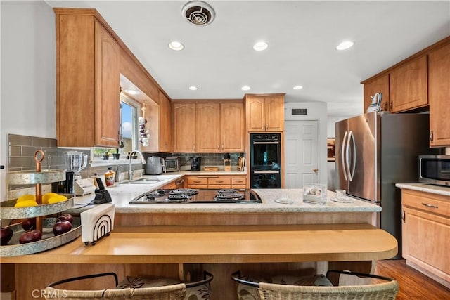 kitchen with sink, a breakfast bar area, appliances with stainless steel finishes, kitchen peninsula, and backsplash