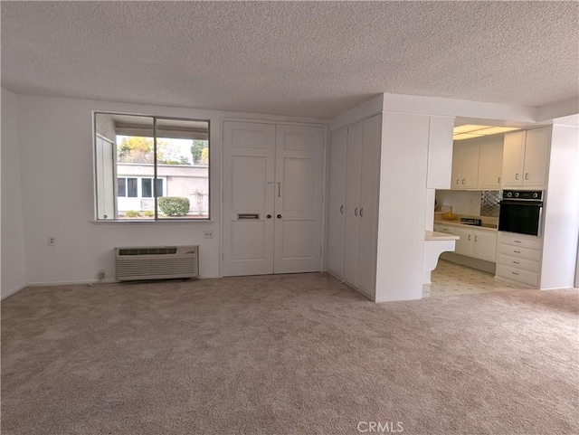 unfurnished living room with a wall mounted air conditioner, light carpet, and a textured ceiling