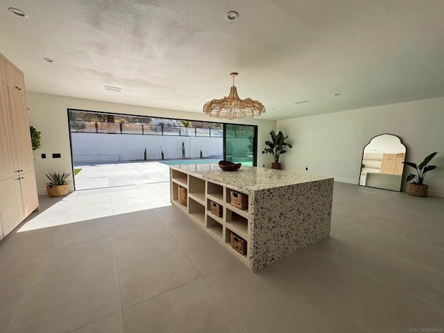 interior space with decorative light fixtures, a center island, a textured ceiling, light tile patterned floors, and light stone countertops