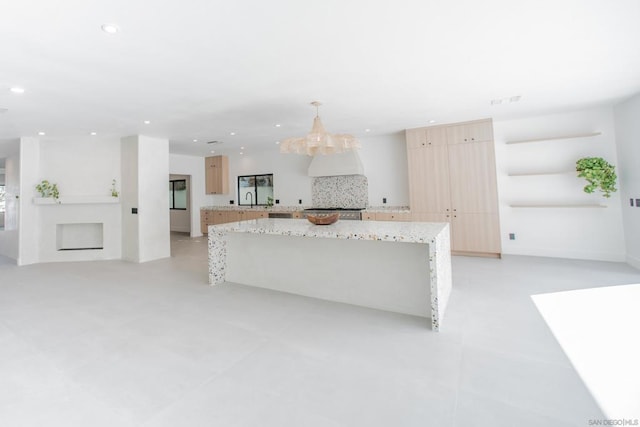 kitchen featuring decorative light fixtures, light stone countertops, a kitchen island, and light brown cabinetry