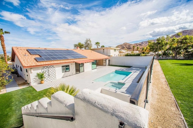 back of house with solar panels, a lawn, a mountain view, a swimming pool with hot tub, and a patio