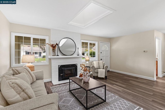 living room featuring dark hardwood / wood-style floors, a skylight, and a brick fireplace