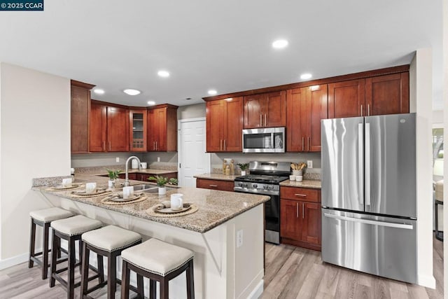 kitchen with a breakfast bar area, light stone counters, kitchen peninsula, stainless steel appliances, and light wood-type flooring