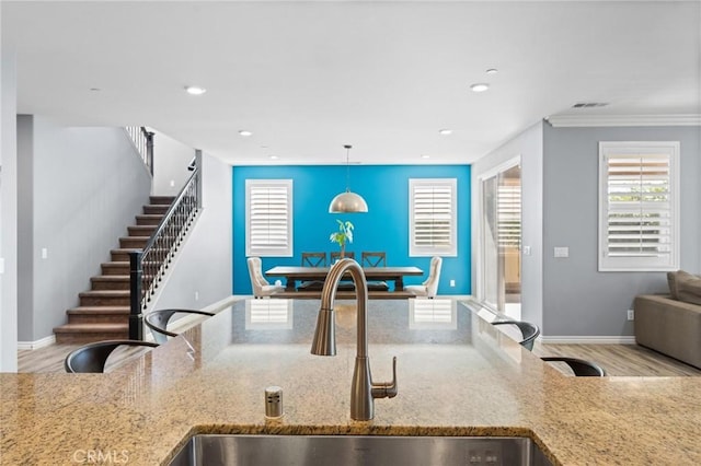 kitchen with light hardwood / wood-style floors, sink, light stone countertops, and hanging light fixtures