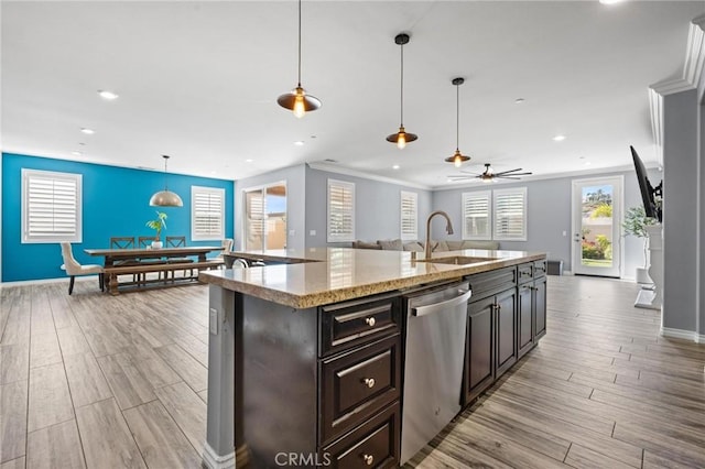 kitchen featuring pendant lighting, dishwasher, sink, a kitchen island with sink, and light wood-type flooring