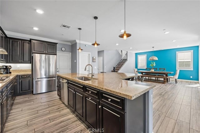 kitchen with sink, hanging light fixtures, a center island with sink, appliances with stainless steel finishes, and light stone countertops