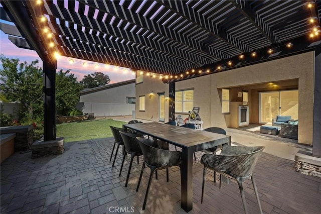 patio terrace at dusk featuring a pergola and a lawn