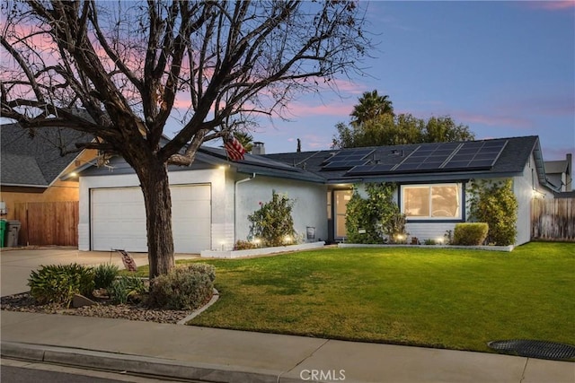 ranch-style home featuring solar panels, concrete driveway, a lawn, an attached garage, and fence