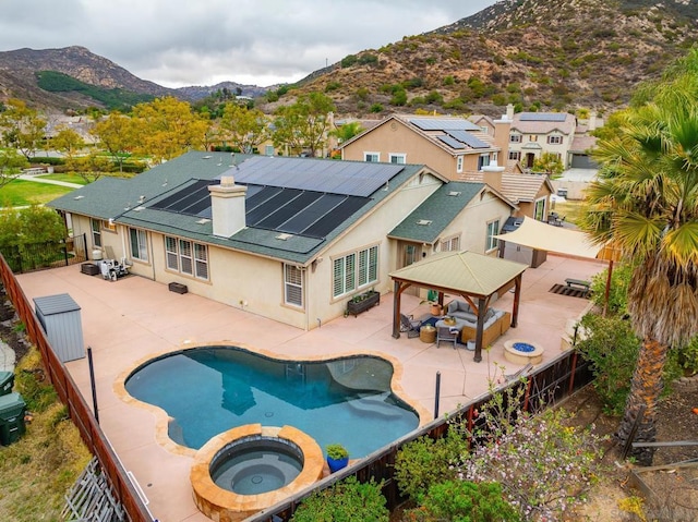 back of property with a swimming pool with hot tub, a gazebo, solar panels, a mountain view, and an outdoor hangout area