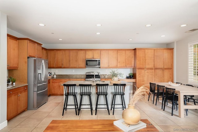 kitchen with appliances with stainless steel finishes, sink, a kitchen breakfast bar, light tile patterned floors, and a center island with sink