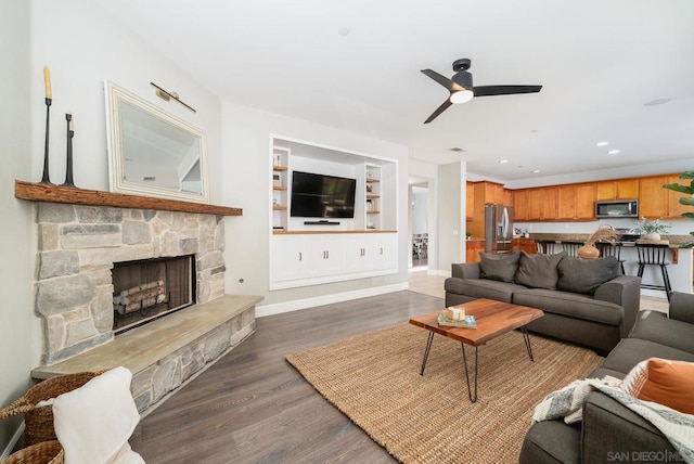 living room featuring dark hardwood / wood-style flooring, a stone fireplace, and ceiling fan