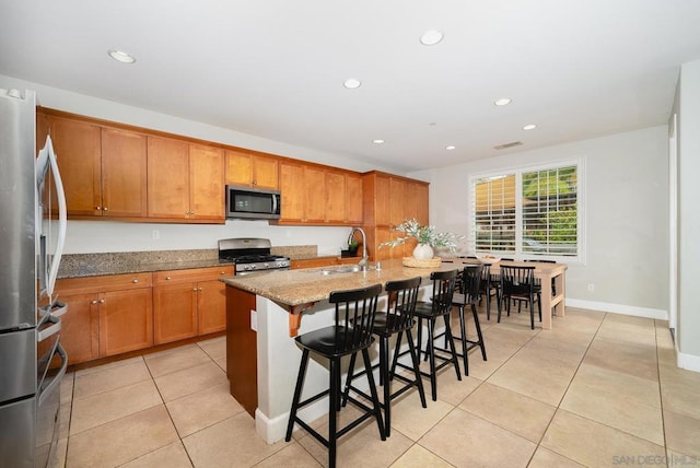 kitchen featuring sink, a breakfast bar area, appliances with stainless steel finishes, light stone counters, and a center island with sink