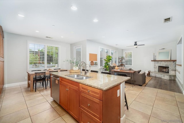 kitchen featuring sink, light tile patterned floors, dishwasher, light stone counters, and an island with sink