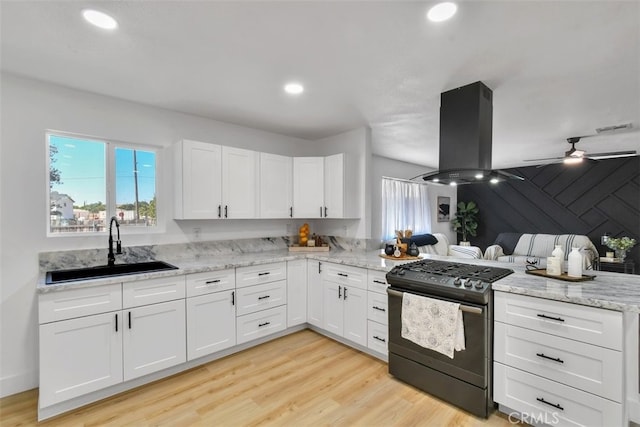 kitchen featuring sink, gas range, light hardwood / wood-style flooring, island exhaust hood, and white cabinets