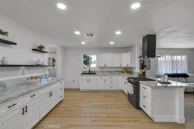 kitchen featuring white cabinetry, light stone counters, island range hood, gas stove, and light wood-type flooring