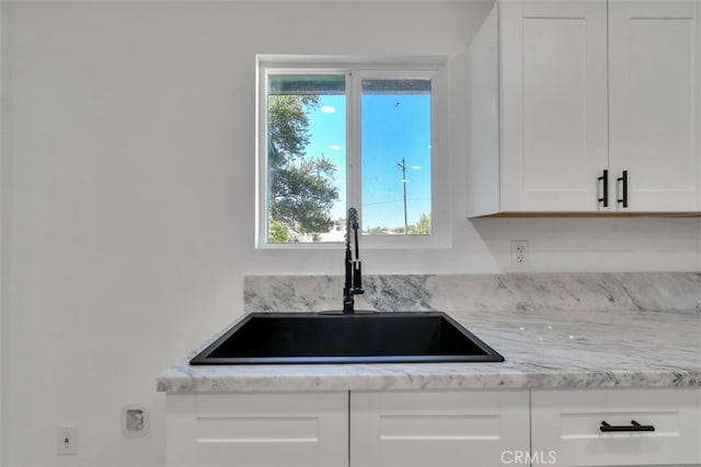 kitchen with light stone countertops, sink, and white cabinets