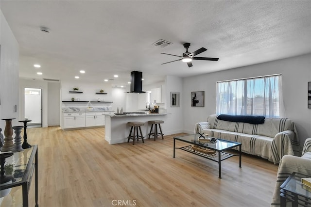 living room featuring ceiling fan, sink, a textured ceiling, and light hardwood / wood-style floors