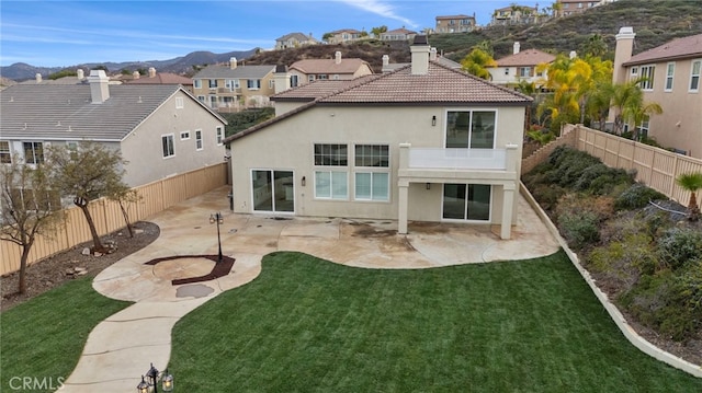 rear view of property featuring a mountain view, a lawn, a patio, and a balcony