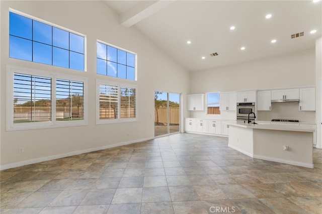 kitchen featuring high vaulted ceiling, an island with sink, white cabinets, oven, and beamed ceiling