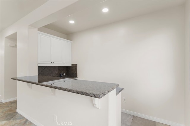 kitchen featuring backsplash, kitchen peninsula, a breakfast bar, and white cabinets