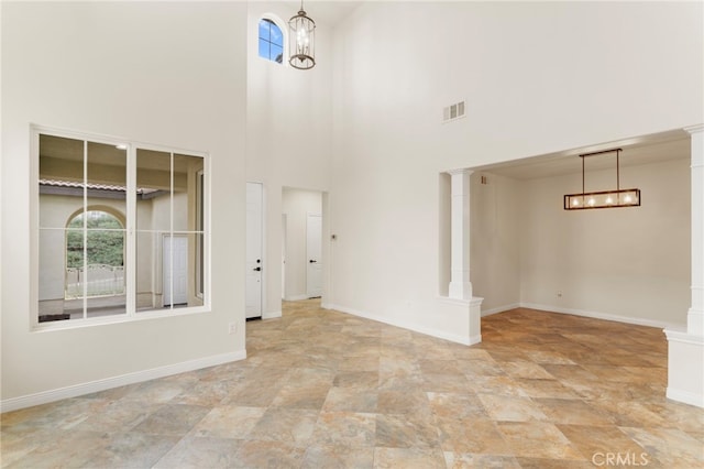 unfurnished room featuring ornate columns and an inviting chandelier