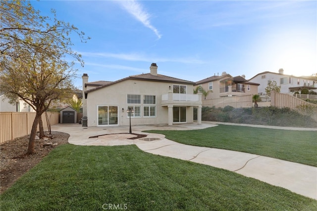 back of property with a balcony, a storage unit, a yard, and a patio area