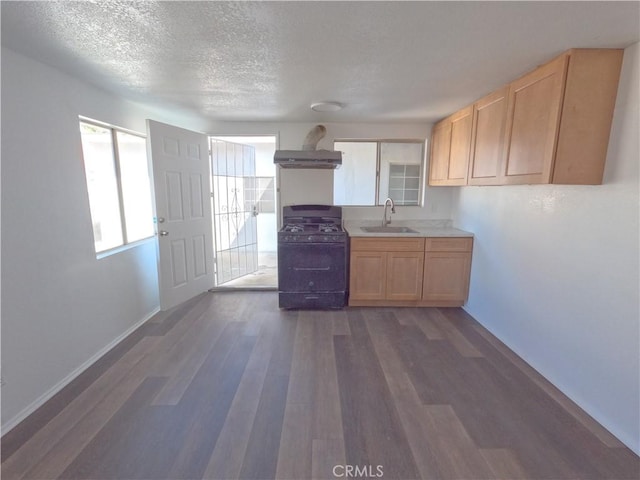 kitchen featuring black gas range oven, sink, wall chimney range hood, dark wood-type flooring, and light brown cabinets