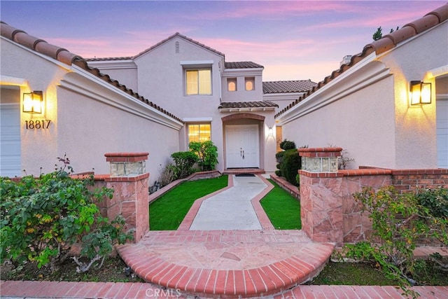 exterior entry at dusk featuring a patio area, a tiled roof, and stucco siding