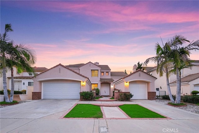 mediterranean / spanish house with a garage, driveway, a tiled roof, and stucco siding