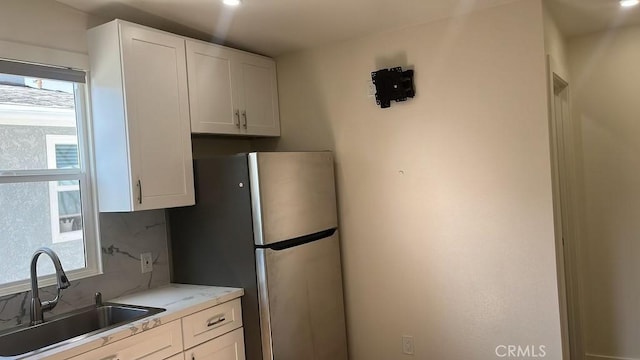 kitchen featuring tasteful backsplash, sink, white cabinets, and stainless steel refrigerator