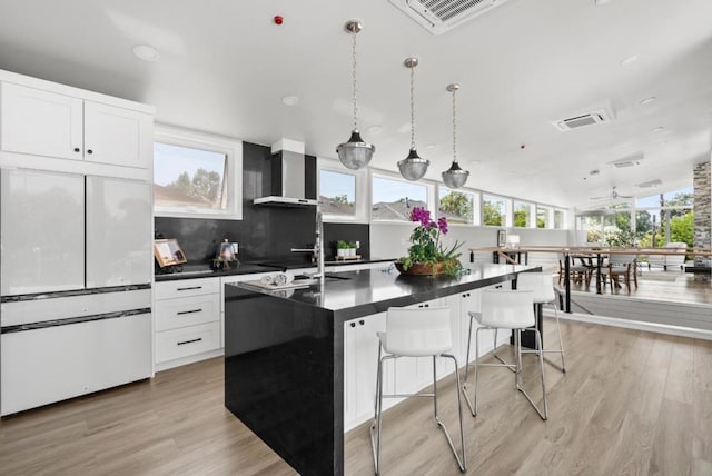 kitchen with a breakfast bar area, paneled built in refrigerator, white cabinetry, hanging light fixtures, and an island with sink