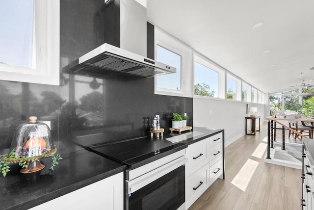 kitchen featuring stainless steel electric stove, vaulted ceiling, white cabinets, light wood-type flooring, and wall chimney exhaust hood