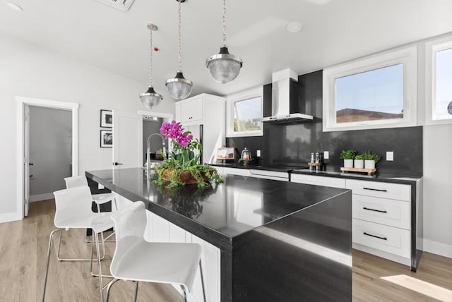 kitchen featuring white cabinetry, a breakfast bar area, a kitchen island with sink, and wall chimney range hood