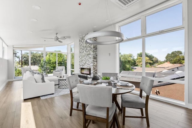 dining space with a stone fireplace, ceiling fan, and light wood-type flooring