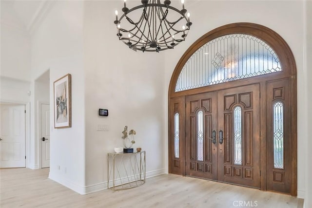 entryway with a towering ceiling, light hardwood / wood-style flooring, and a chandelier